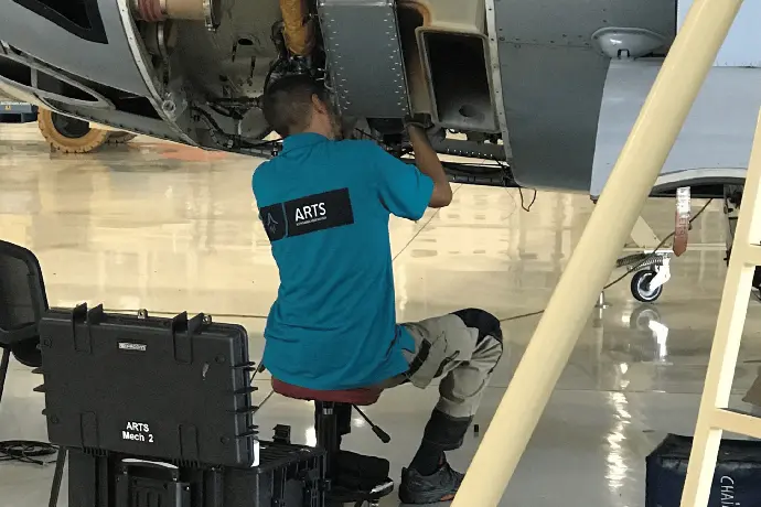 Professional aircraft mechanics in protective clothing working collaboratively to service the engine and wing components of a large aircraft indoors